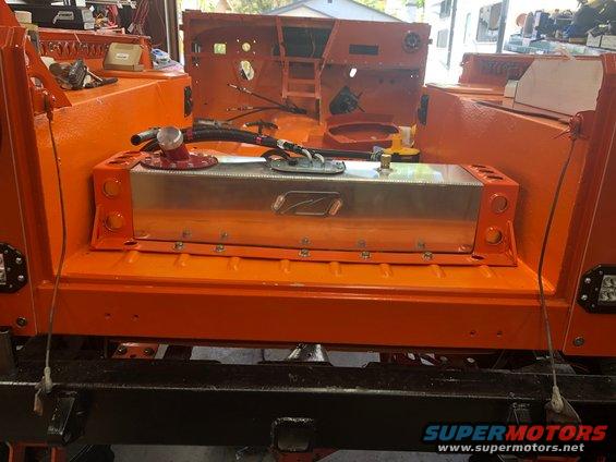 Custom aluminum fuel tank with red cap and fuel lines installed in an orange-painted vehicle body