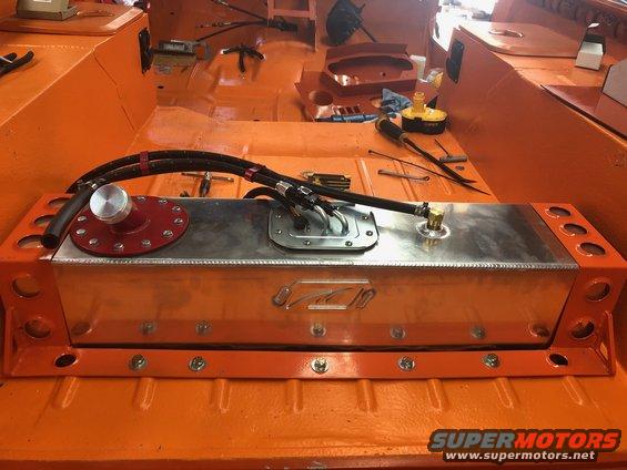 Aftermarket aluminum fuel tank with red cap and braided fuel lines installed in an orange interior