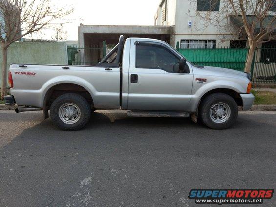 Silver Ford F-250 pickup truck with a roll bar in the bed. Turbo badging on the fender