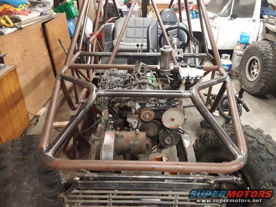 Custom buggy frame with exposed engine, seats, and steering wheel. Large tires visible