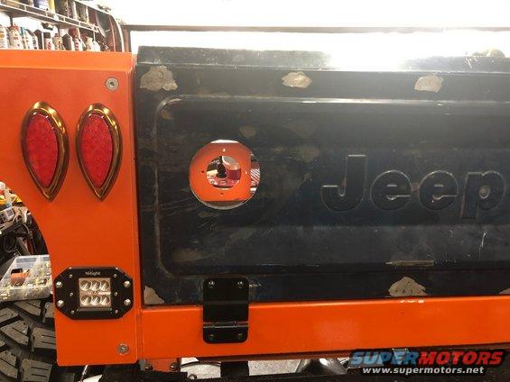 Orange fender with dual red taillights next to black Jeep tailgate with circular cutout