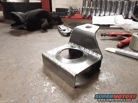 custom metal bracket with circular cutout and visible welds, on a workbench with tools