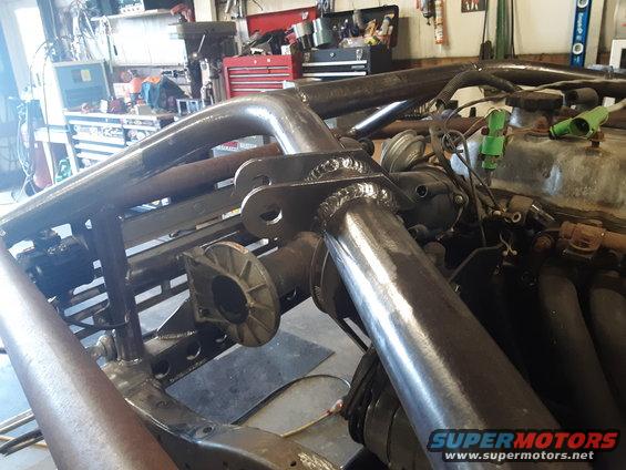 Custom roll cage being welded onto a vehicle frame, showing engine components
