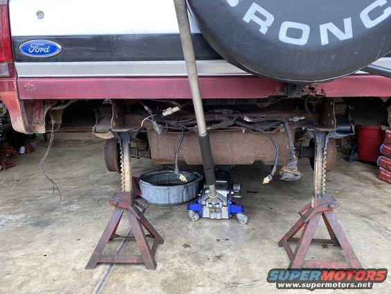 Red and silver Ford Bronco rear end on jack stands with exposed undercarriage and wiring
