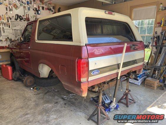 1994 Ford Bronco rear end disassembled, supported by jack stands in a garage. Rear axle removed