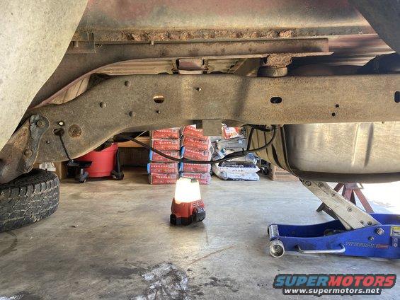 underbody of a truck with a fuel tank and frame visible, being worked on with a jack