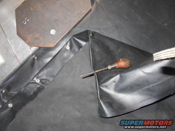Close-up of black textured material being attached with rivets and a screwdriver