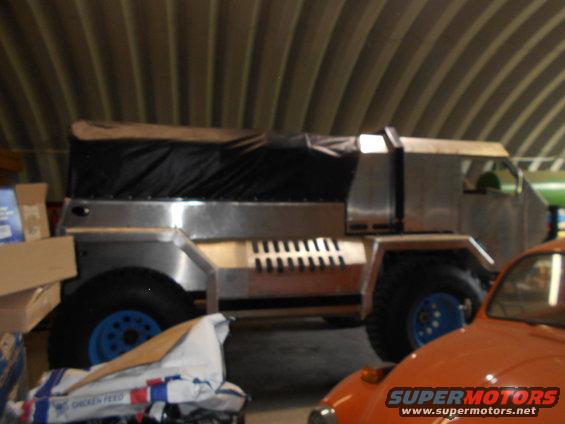 Custom truck with aluminum body and canvas top parked next to an orange car