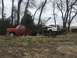 1981 Ford F-350 - A red tow truck hauls a damaged white pickup truck on a trailer in a field.