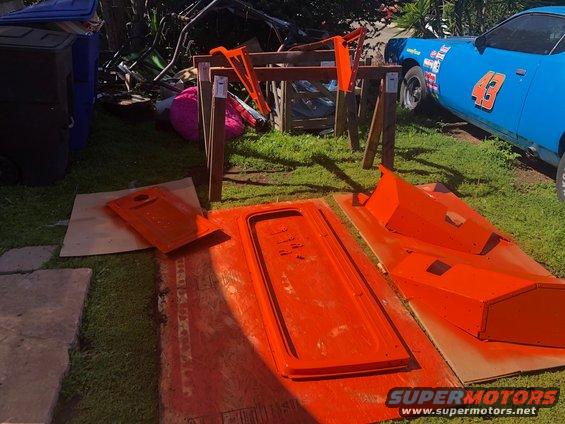 Orange painted car doors and panels laid out on grass next to a blue race car with number 43