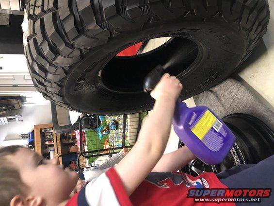 Child spraying a large off-road tire with a purple bottle