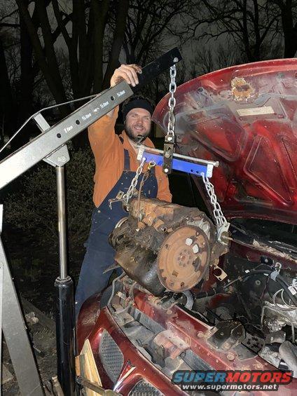 Guy using engine hoist to remove an engine from a red car