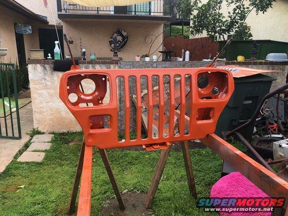 Orange Jeep Wrangler grille on sawhorses outdoors, showing headlight openings and vertical grille slats