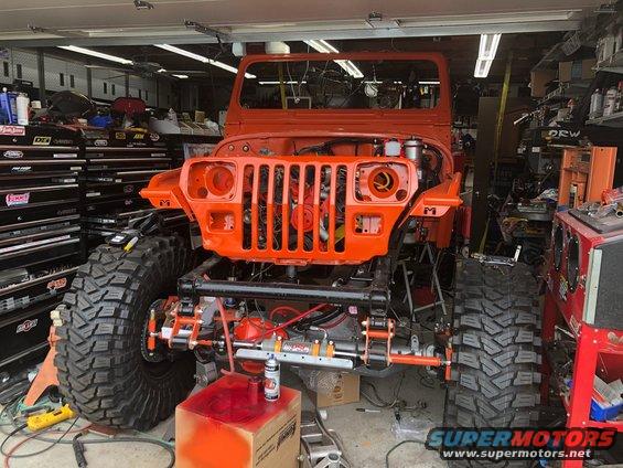 Orange Jeep Wrangler with lifted suspension and large tires in a garage