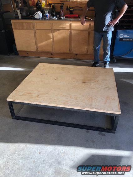 Plywood platform on a black metal frame in a garage setting