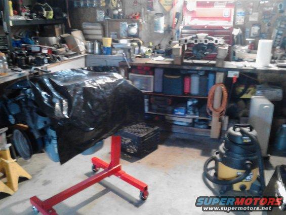 Engine on a red engine stand covered in a black tarp in a cluttered garage