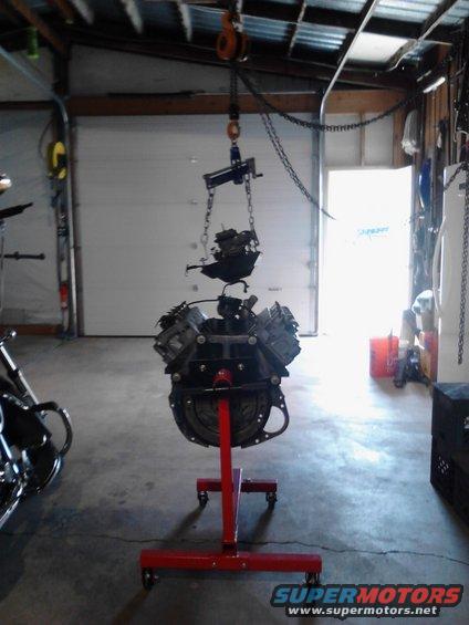 Engine assembly suspended from a hoist and resting on a red engine stand in a garage