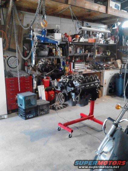 engine on a red stand in a garage, with tools and shelves in background