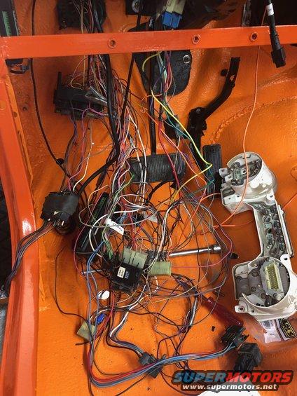 Orange vehicle interior with tangled orange, black, yellow, and blue wires and a detached dashboard instrument cluster