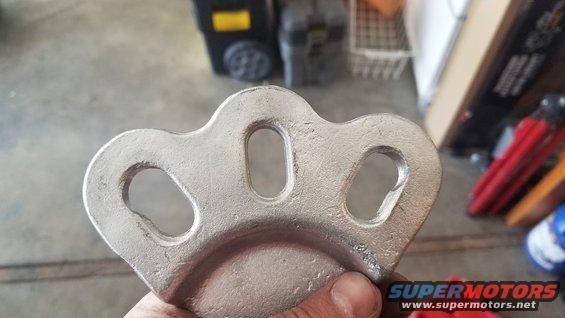 Metal part with three oval holes held in hand, with a Supermotors logo in the corner