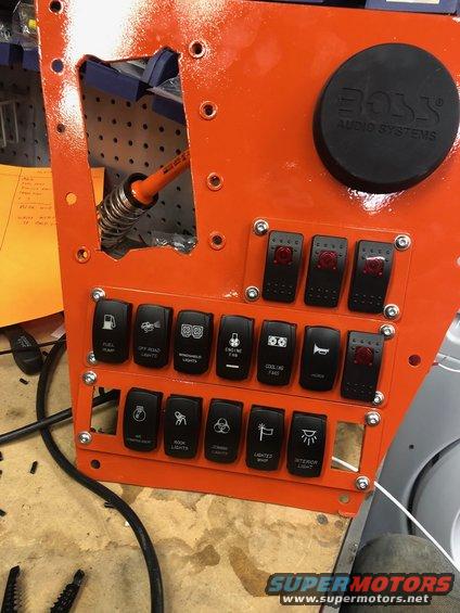 Orange custom switch panel with multiple toggle switches labeled for various functions and a BOSS AUDIO SYSTEMS cap