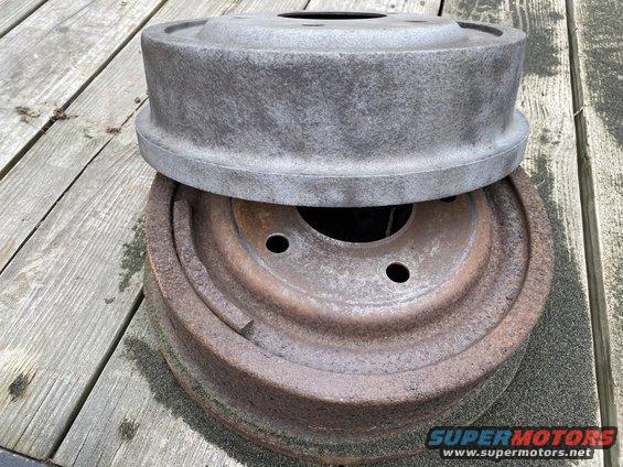 Two drum brake assemblies stacked on a wooden deck. One is rusty, the other is gray