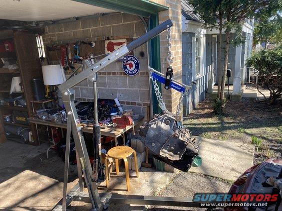 Transmission being lifted by an engine hoist in front of a garage