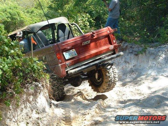 1986 Ford Bronco with soft top, driving on a sandy trail with one wheel off the ground