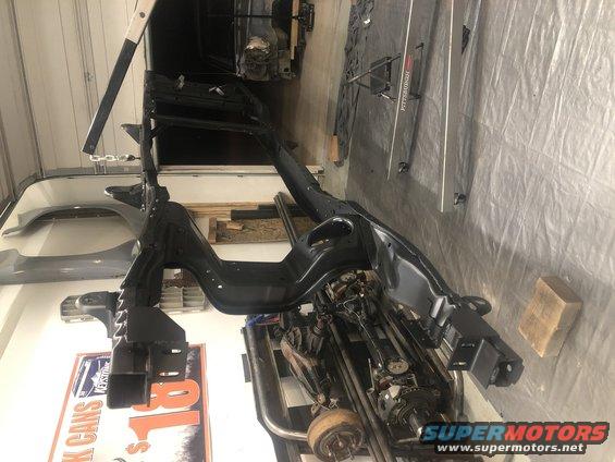 Black vehicle frame and suspension components suspended from a hoist, with parts of a differential visible