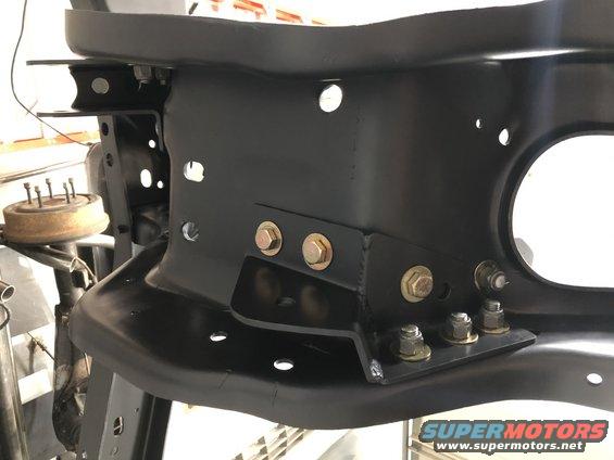 Black painted metal frame bracket with multiple bolts and holes, part of a vehicle's chassis