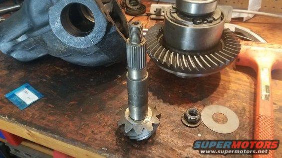 Differential gears, pinion shaft, and housing parts laid out on a workbench. Includes a nut and washer