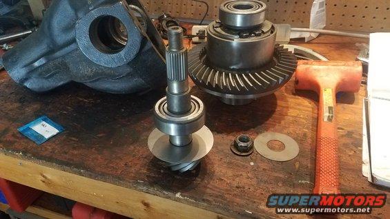 Differential gears, pinion shaft with bearings, and housing on a workbench with a rubber mallet