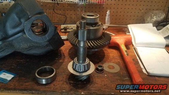 Differential gears, bearings, and housing on a workbench with a hammer and notebook