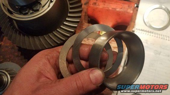Hand holding several metal shims with a differential gear in the background