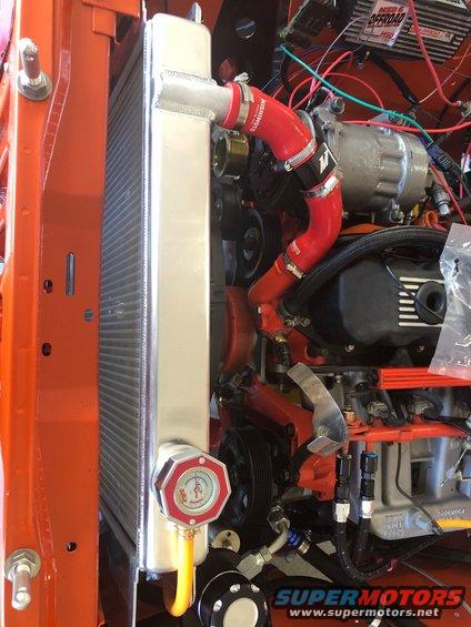 Engine bay showing aluminum radiator, red silicone hoses, AC compressor, and wiring. SuperMotors logo visible