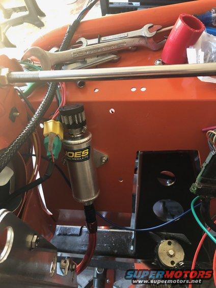 Engine bay with orange panel, silver canister, and tools. Wires and hoses are visible
