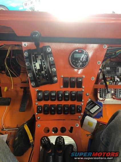 Orange dashboard with a black automatic gear shifter, numerous toggle switches, and a digital gauge