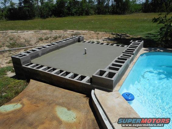 Concrete pool deck under construction with cinder blocks and fresh cement, next to a blue swimming pool