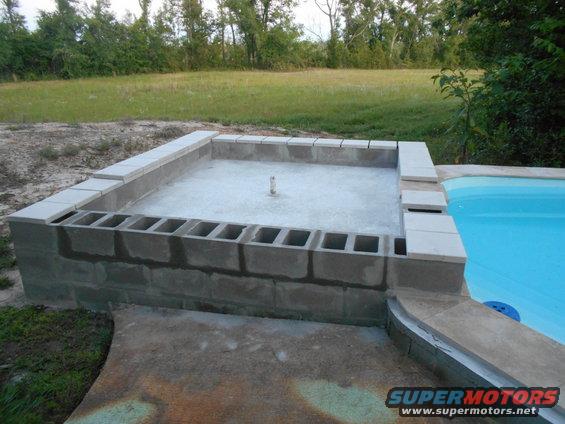 Concrete block structure and pool under construction next to a grassy field