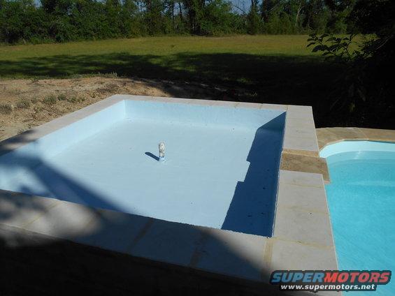 Empty swimming pool with a pipe in the center, next to a filled pool