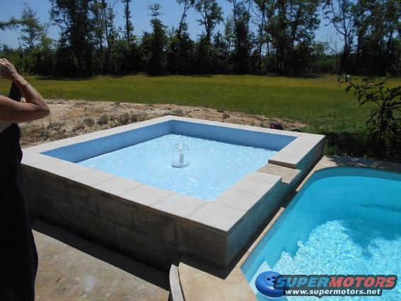 Two pools, one square with a fountain, next to a kidney-shaped pool. Person holding a phone in the foreground