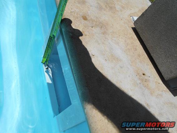 Pool edge with a green measuring tape showing water depth, concrete deck, and a dark shadow