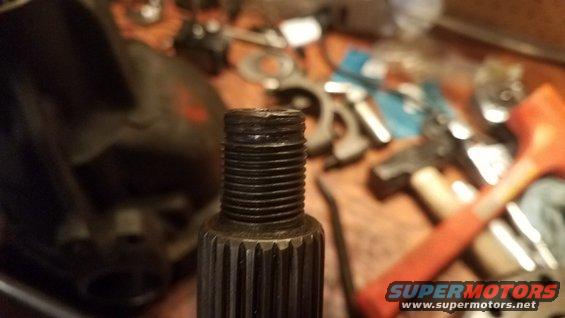 Close-up of a threaded shaft with splines, surrounded by tools on a workbench