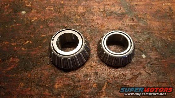 Two tapered roller bearings on a wooden surface. One bearing is larger than the other