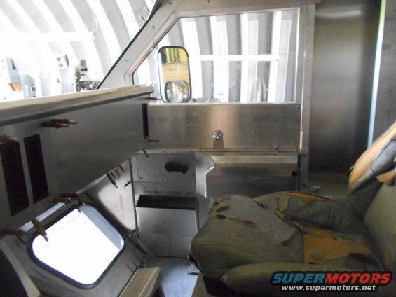 Interior of a vehicle cockpit with a torn seat, dashboard, and side mirror.