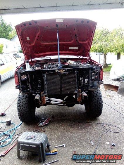 Red SUV front view, hood open, grille removed, large tires, outdoors