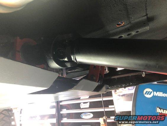 Underside view of a driveshaft and skid plate, with a Miller welder in the background
