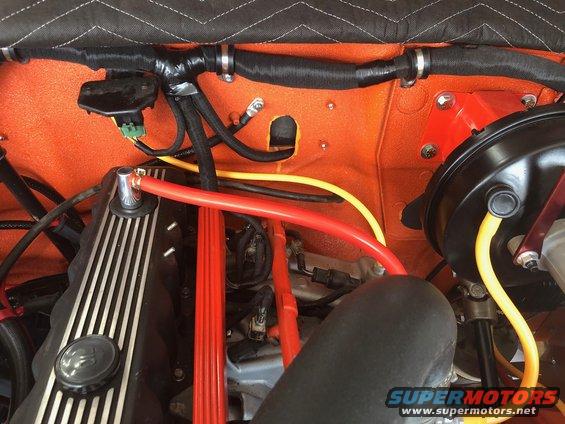 Engine bay showing orange firewall, black hoses, red and yellow wires, and part of a black air intake