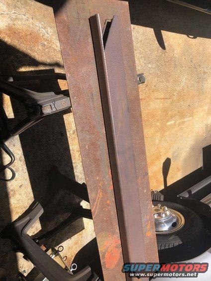 Rusty metal plates and brackets on concrete floor, with a tire and hubcap visible