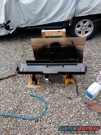 Metal part on jack stands, being painted. A car is covered in the background